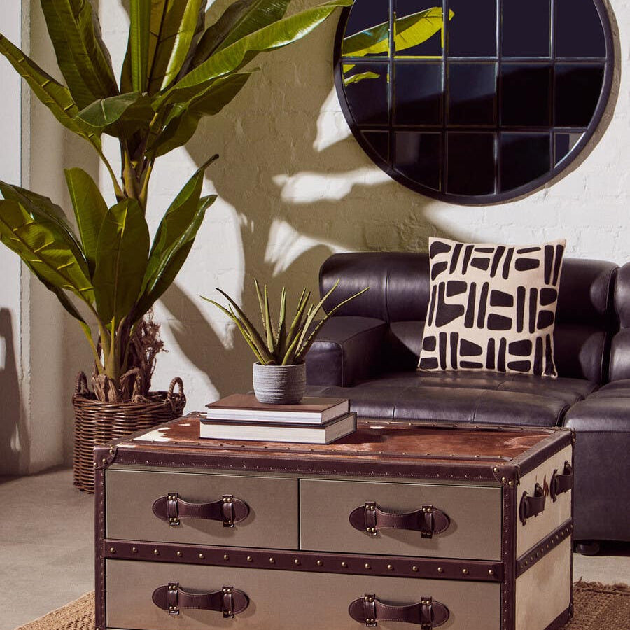 Antique black left arm leather modular chaise sofa with a sleek design, featuring plush cushions and a modern aesthetic. The sofa is positioned near a round mirror and a potted plant, creating a stylish living space. A decorative throw and patterned pillows add texture and comfort to the seating area