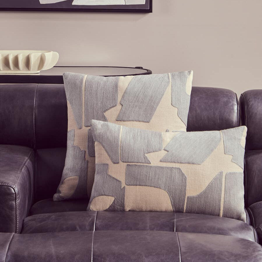 Left arm leather modular chaise sofa in antique black with two decorative pillows featuring a geometric pattern in beige and gray, set against a neutral wall with a framed artwork in the background