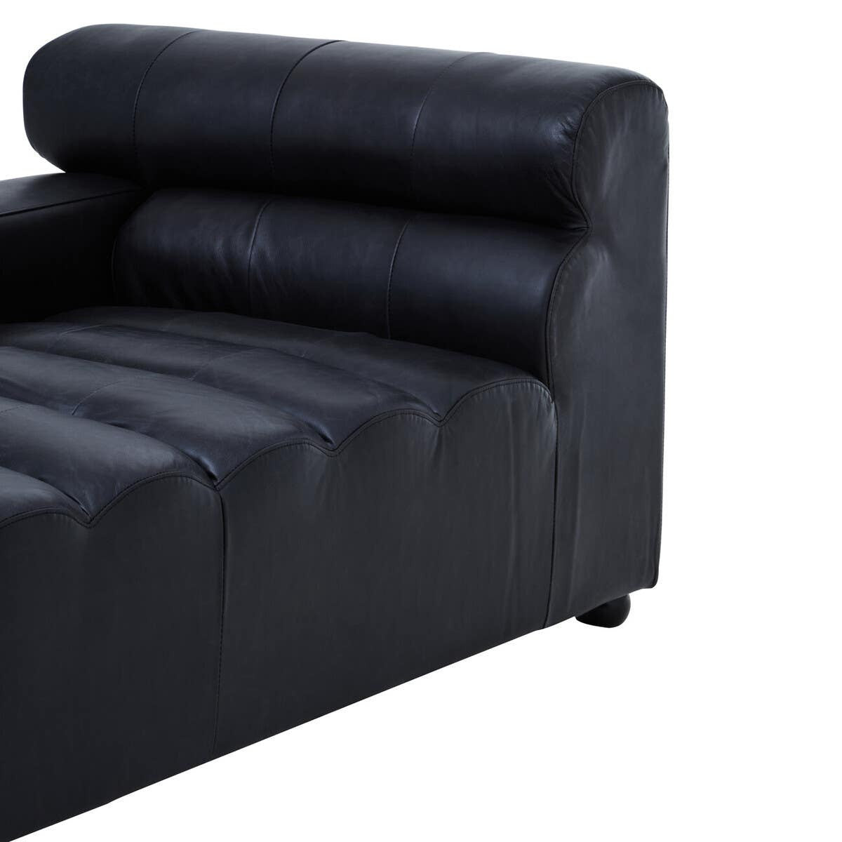 Left arm of a modular chaise sofa upholstered in antique black leather, featuring a tufted design on the seat and a rounded backrest for added comfort. The sofa has a sleek, modern appearance with a low profile and sturdy base