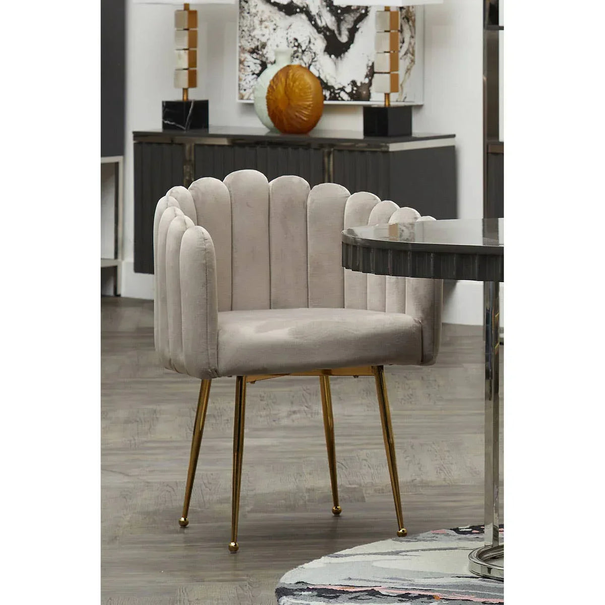 Beige velvet accent chair with scalloped backrest and gold metal legs beside round dining table