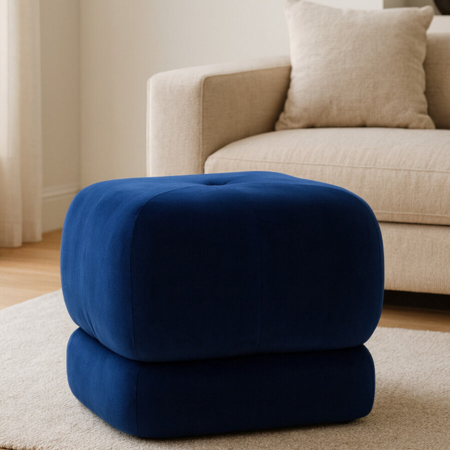 Midnight blue velvet square stool with a soft, plush texture, positioned on a light-colored rug in a cozy living room setting, next to a beige sofa with decorative pillows
