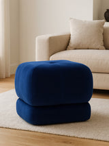 Midnight blue velvet square stool with a soft, plush texture, positioned on a light-colored rug in a cozy living room setting, next to a beige sofa with decorative pillows