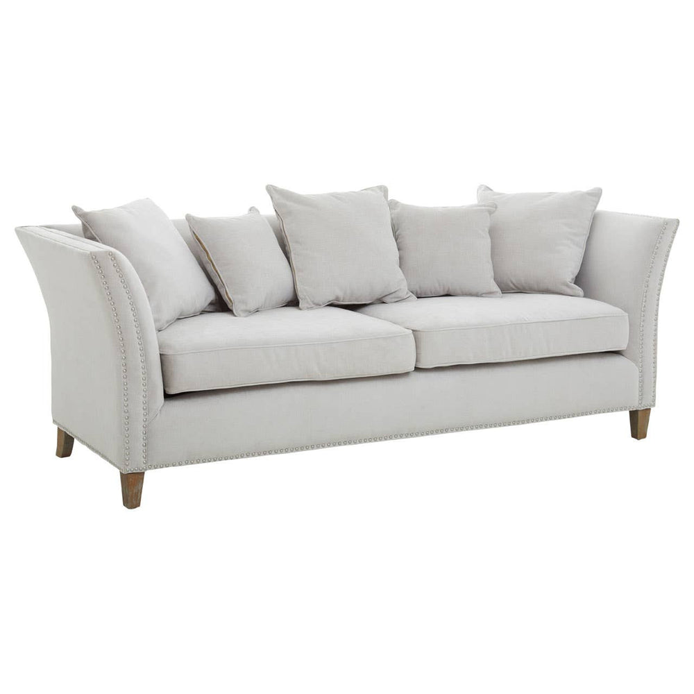 Three-seat sofa upholstered in light grey fabric, featuring a curved backrest and armrests. The sofa is adorned with several plush cushions for added comfort and is supported by wooden legs