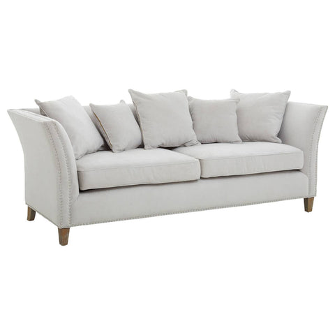Three-seat sofa upholstered in light grey fabric, featuring a curved backrest and armrests. The sofa is adorned with several plush cushions for added comfort and is supported by wooden legs