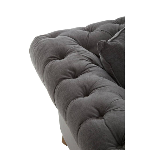 Grey fabric sofa with a tufted design, featuring a plush seat and armrest. The corner of the sofa shows a soft texture and rounded edges, highlighting its modern style