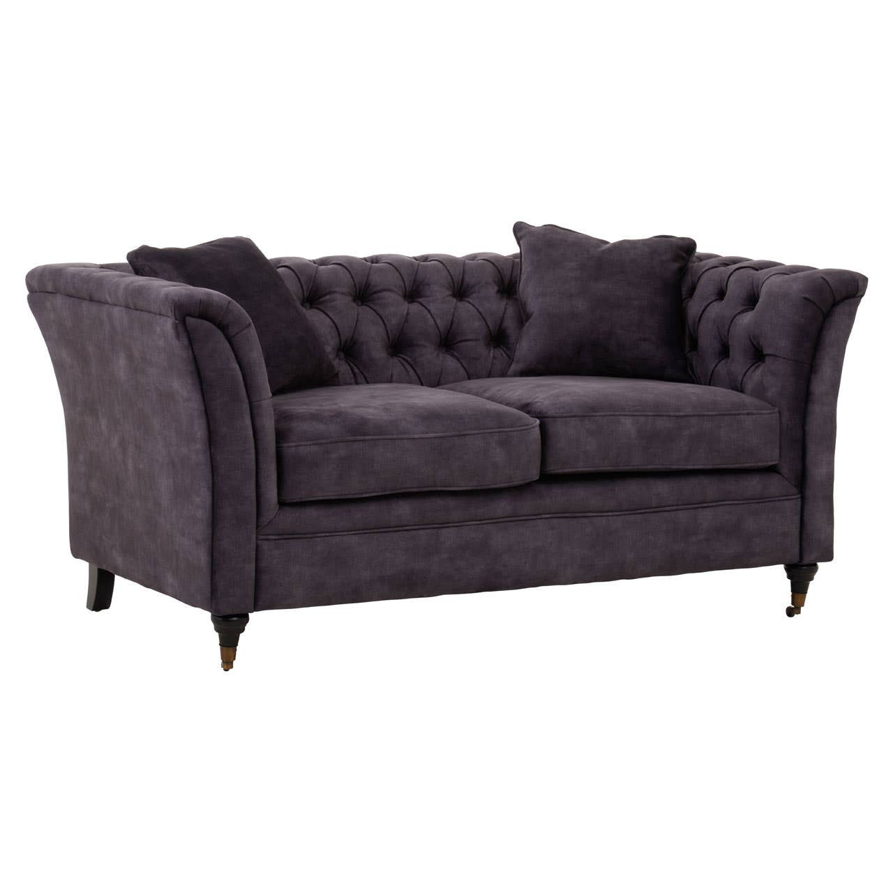 Two-seat sofa upholstered in grey velvet with a tufted backrest, featuring rounded arms and two matching throw pillows. The sofa stands on tapered wooden legs