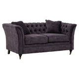 Two-seat sofa upholstered in grey velvet with a tufted backrest, featuring rounded arms and two matching throw pillows. The sofa stands on tapered wooden legs