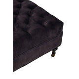Plush dark velvet ottoman with button tufted upholstery and black turned wooden leg