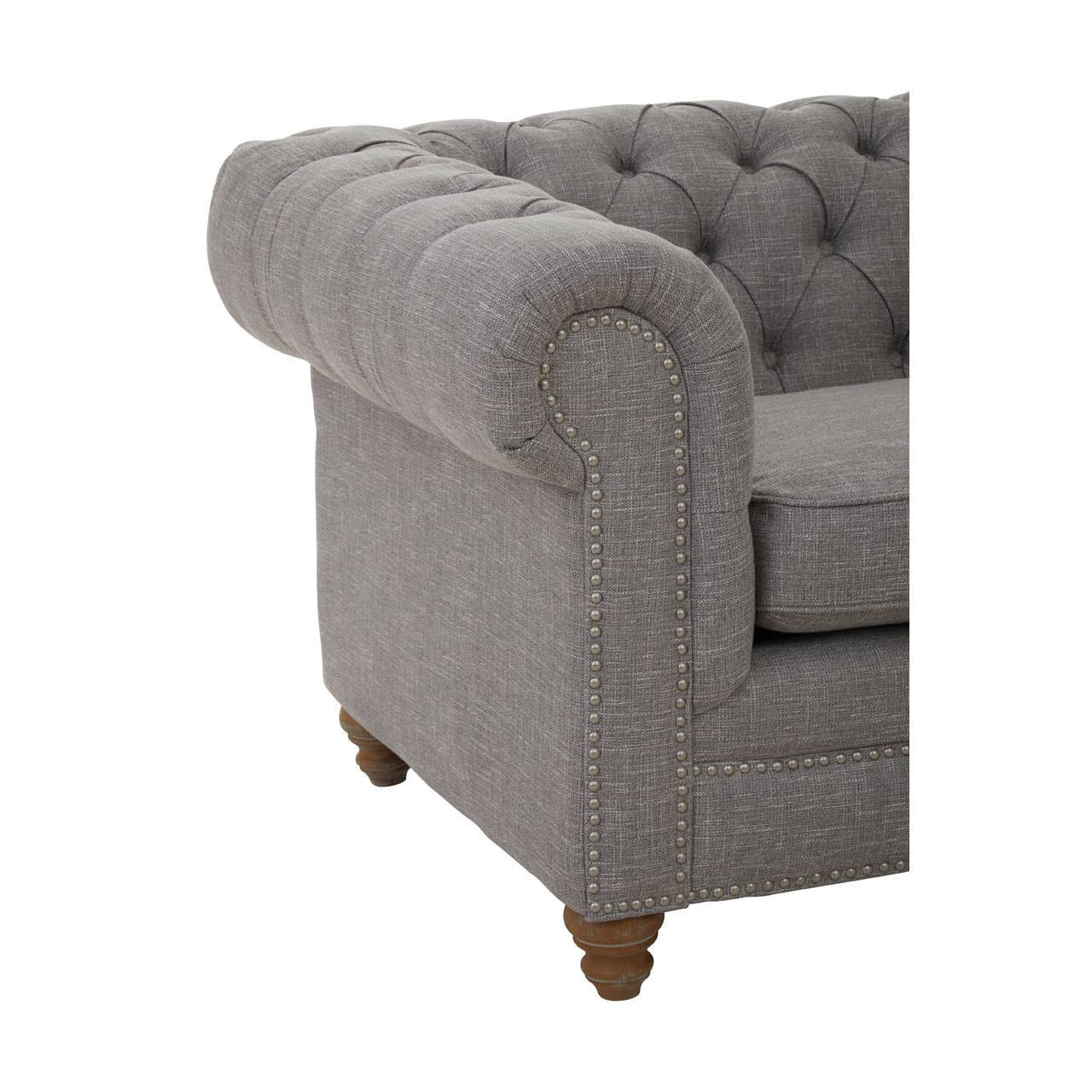 Grey linen sofa with a tufted backrest and rolled arms, featuring wooden legs. The corner of the sofa is visible, showcasing its elegant design and soft fabric texture
