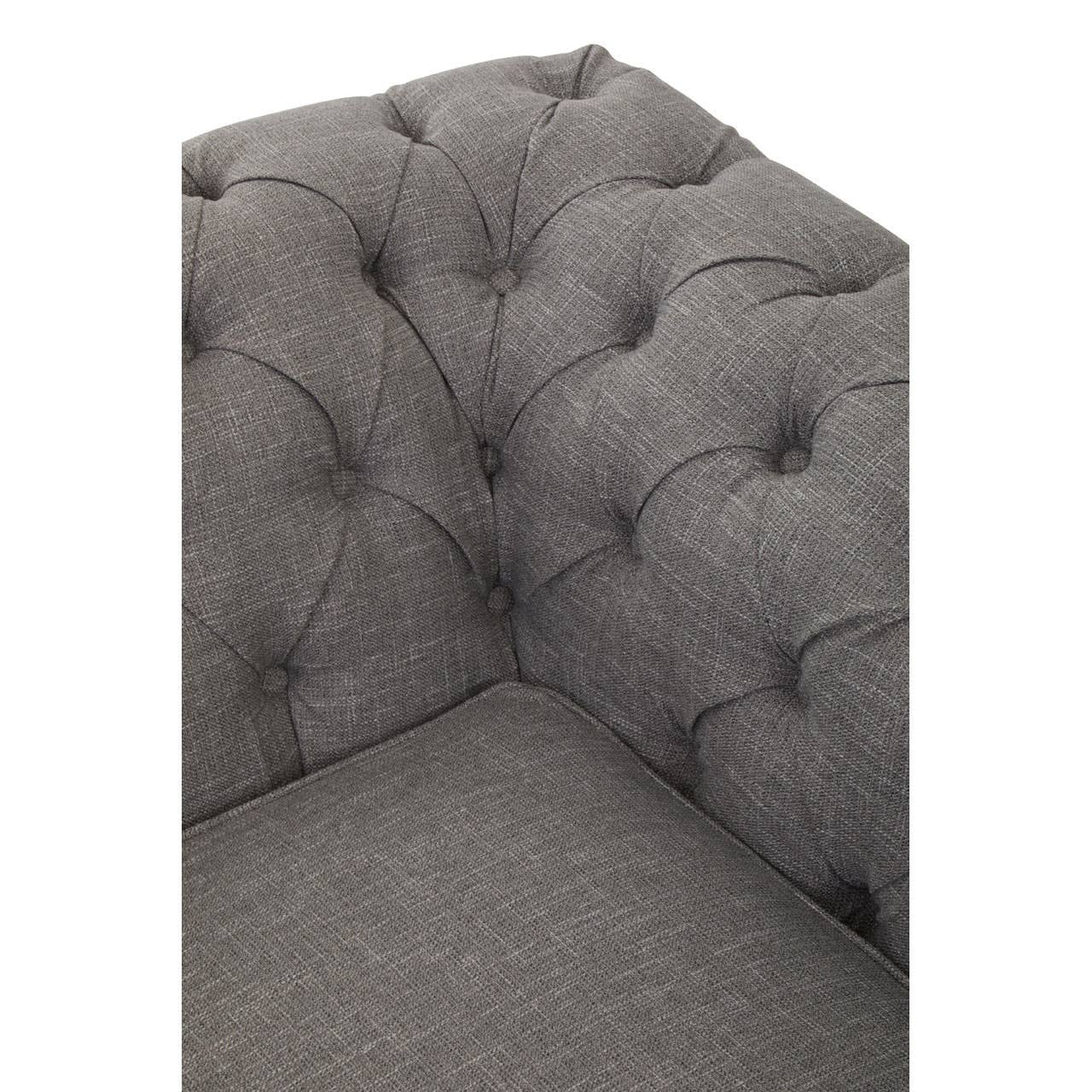 Close-up view of the corner of a two-seat sofa upholstered in grey linen, featuring tufted detailing on the backrest and seat. The fabric has a soft texture, and the overall design appears modern and stylish