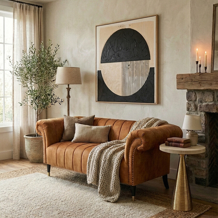 A stylish two-seat sofa upholstered in rich gold velvet, featuring plush cushions and elegant armrests. The sofa is positioned in a cozy living room setting with a large window allowing natural light to fill the space. A textured throw blanket is draped over one arm, and decorative pillows are placed on the seat. Nearby, a small round side table holds a lamp, and a potted plant adds a touch