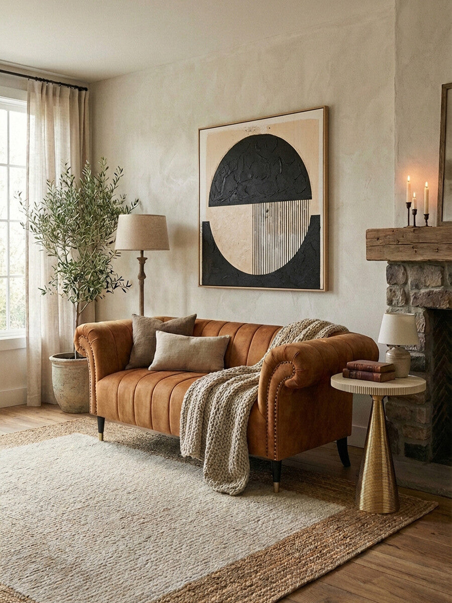A stylish two-seat sofa upholstered in rich gold velvet, featuring plush cushions and elegant armrests. The sofa is positioned in a cozy living room setting with a large window allowing natural light to fill the space. A textured throw blanket is draped over one arm, and decorative pillows are placed on the seat. Nearby, a small round side table holds a lamp, and a potted plant adds a touch
