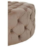 Beige velvet round ottoman stool with tufted detailing, showcasing a soft, plush texture and a rounded shape. The corner of the stool is visible, highlighting its elegant design and neutral color