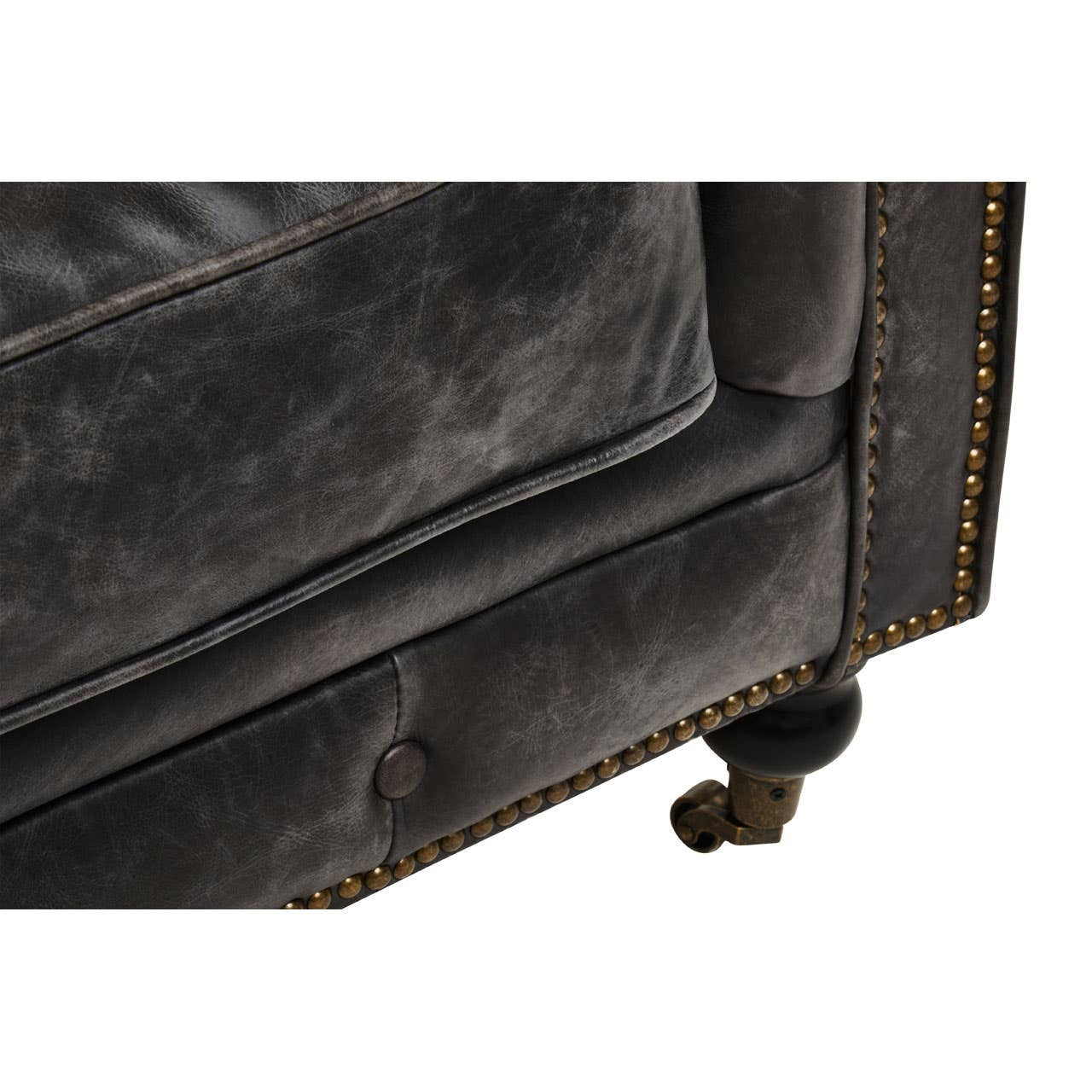 Close-up view of the corner of a Hoxton Antique Black 3 Seat Chesterfield Leather Sofa, showcasing the textured leather upholstery, decorative nailhead trim, and a wooden leg with a wheel for mobility