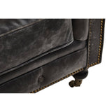 Close-up view of the corner of a Hoxton Antique Black 3 Seat Chesterfield Leather Sofa, showcasing the textured leather upholstery, decorative nailhead trim, and a wooden leg with a wheel for mobility