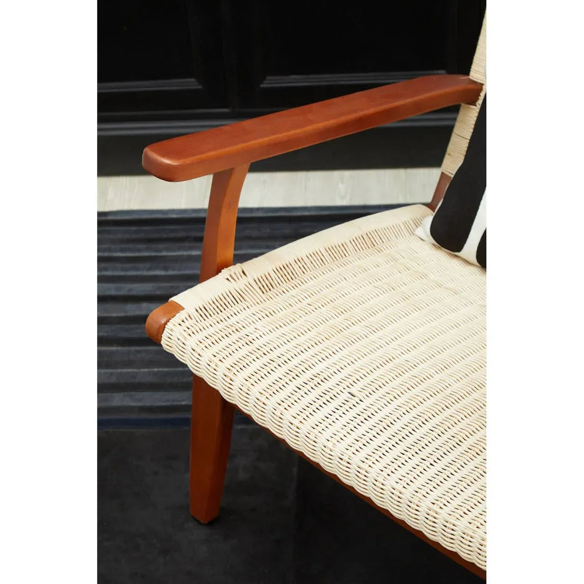 Closeup of wooden armchair with woven rattan seat and striped cushion on dark rug