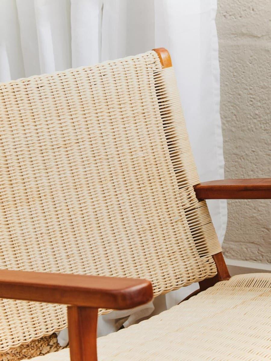 Closeup of natural rattan armchair with wooden arms and woven seat near white curtain