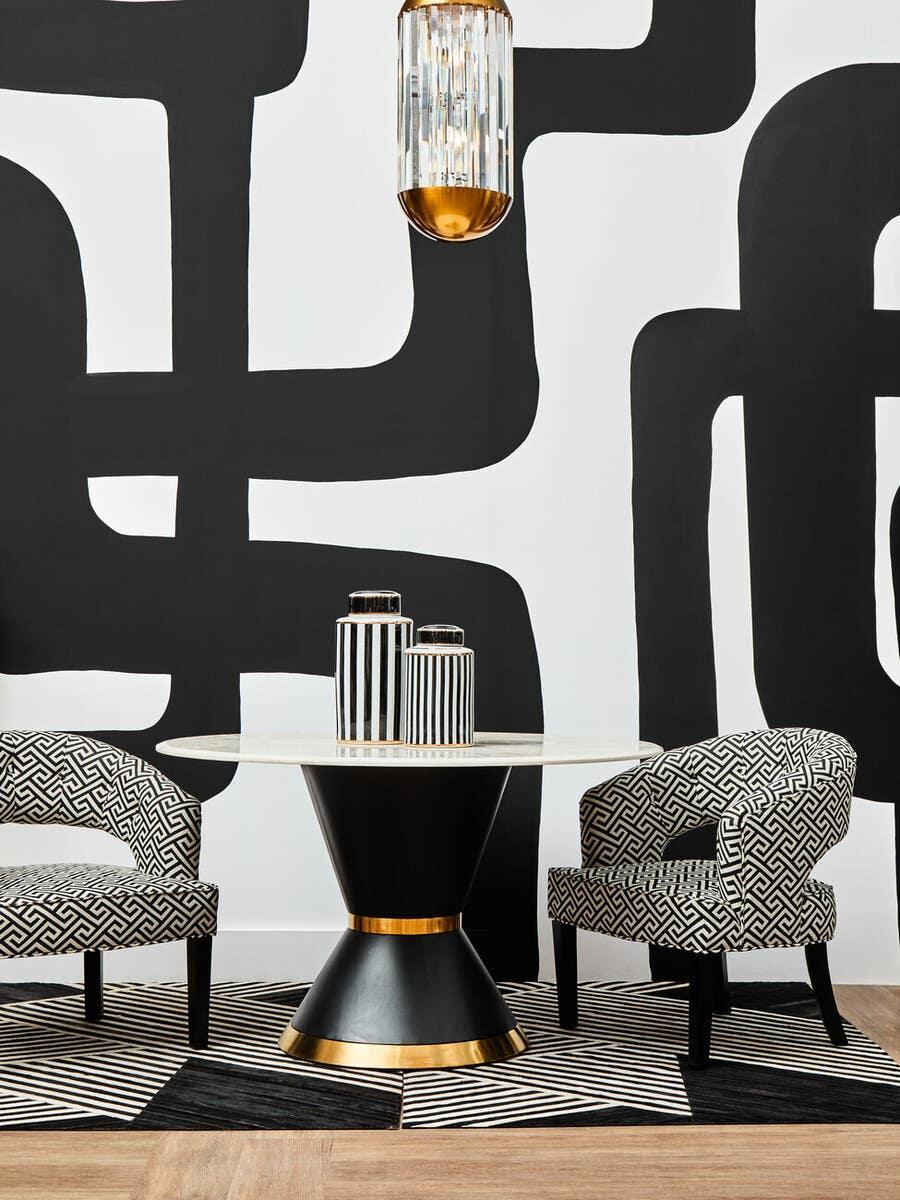 Modern dining table with black base, gold accents and patterned chairs on geometric rug