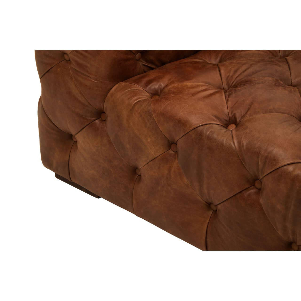 Brown leather upholstery with a tufted design, showcasing the corner and arm of a modern Chesterfield sofa. The texture of the leather is visible, highlighting its rich color and craftsmanship