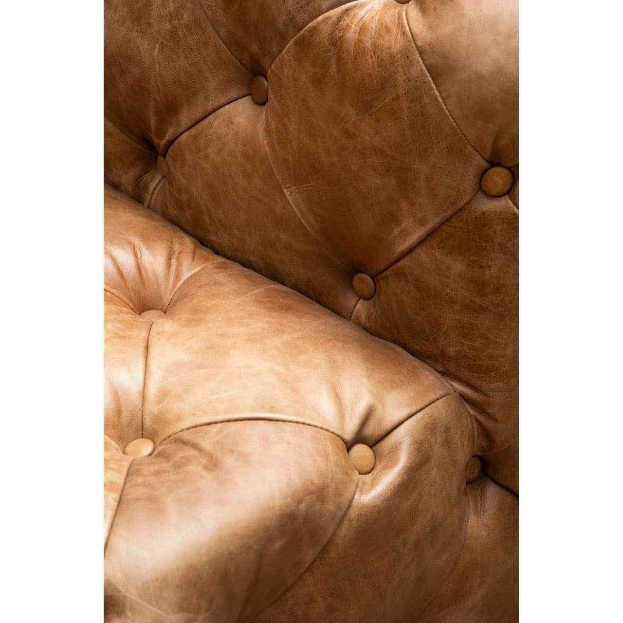 Close-up view of a brown leather Chesterfield sofa chair featuring a tufted design with visible stitching and button details, showcasing the rich texture and warm tones of the leather