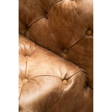 Close-up view of a brown leather Chesterfield sofa chair featuring a tufted design with visible stitching and button details, showcasing the rich texture and warm tones of the leather