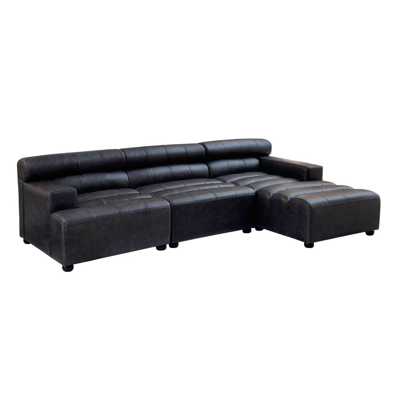 A modular chaise sofa in antique black leather featuring a right arm design, with a sleek, modern silhouette and low-profile backrest. The sofa has a spacious seating area and a chaise extension on the right side, supported by short, sturdy legs