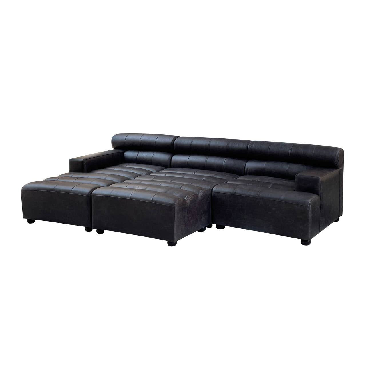 Black leather modular ottoman with a sleek design, featuring a low backrest and plush seating. The ottoman is divided into two sections, providing versatility in arrangement. It rests on short, sturdy legs, enhancing its modern aesthetic
