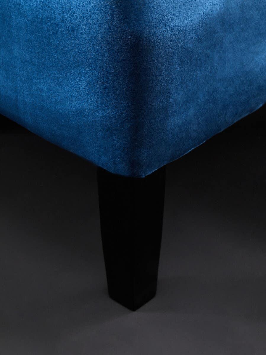 Blue velvet sofa corner with black wooden leg on dark floor