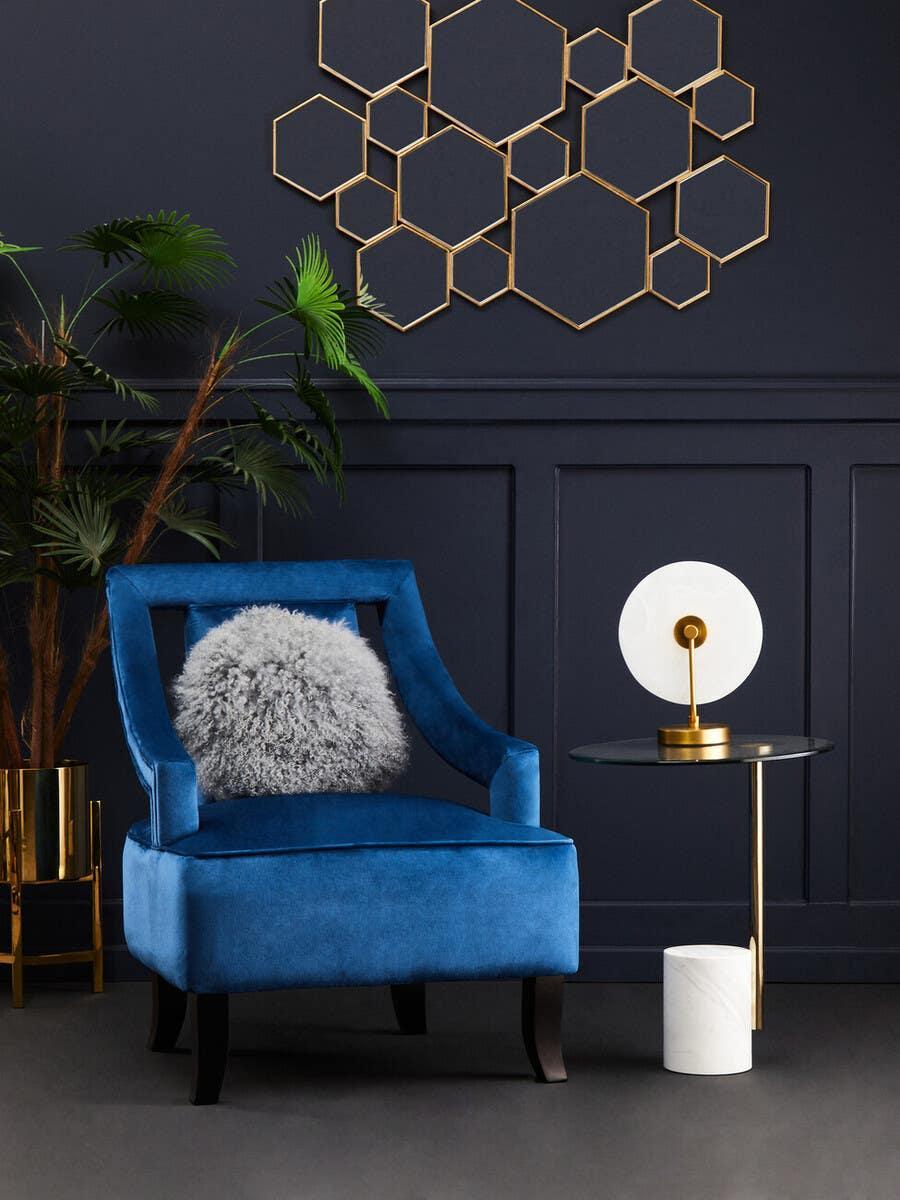 Blue velvet accent chair with grey cushion, glass side table and modern gold wall art