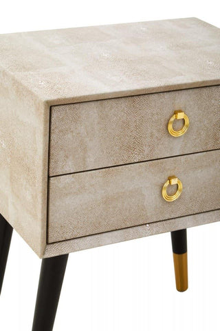 Beige two drawer bedside table with gold ring handles and tapered black and gold legs