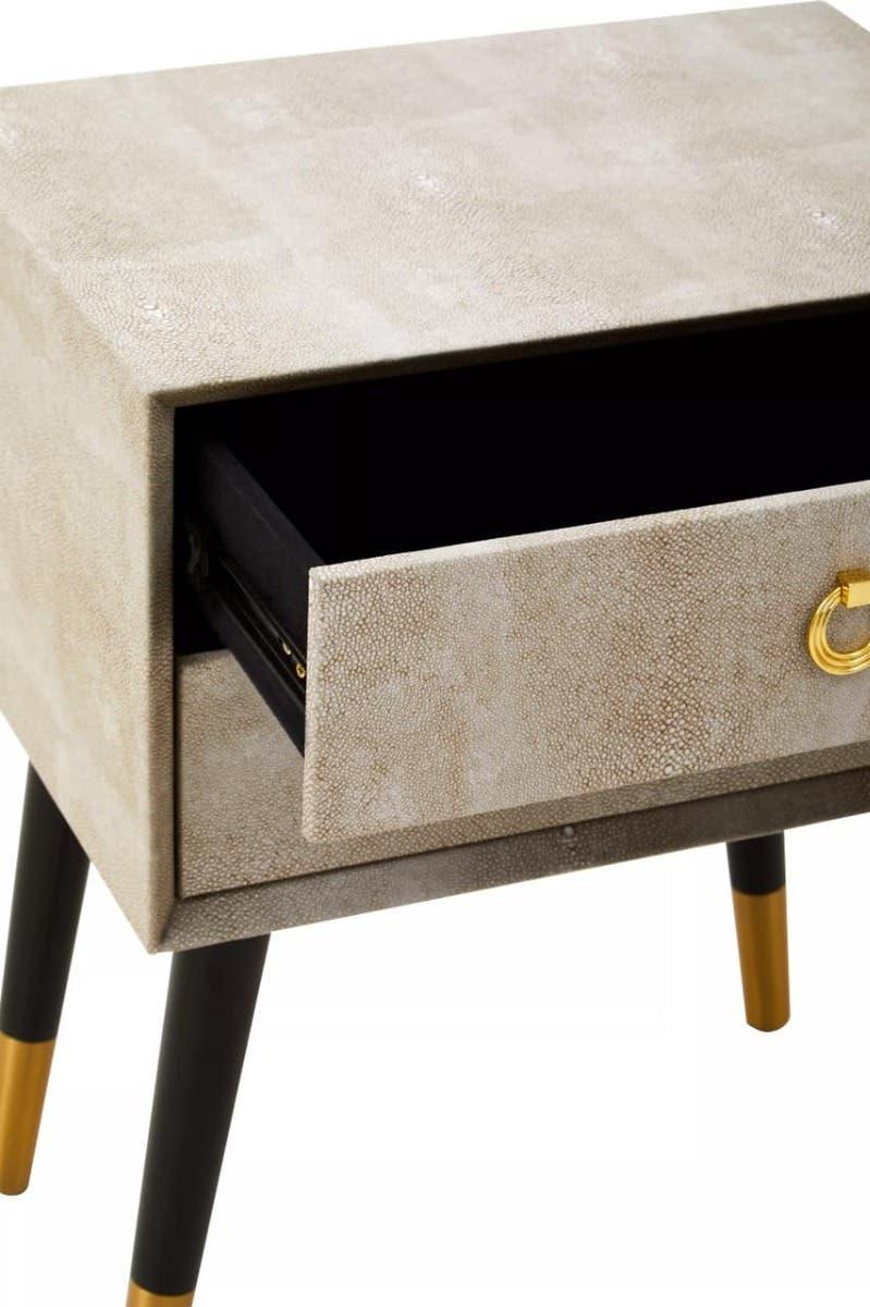 Beige bedside table with textured drawer and gold handle, black tapered legs with gold tips