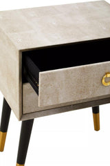 Beige bedside table with textured drawer and gold handle, black tapered legs with gold tips
