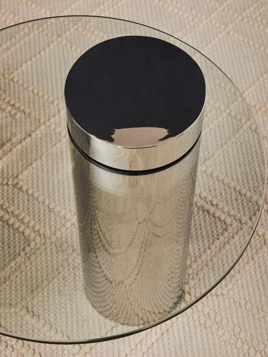 Round glass coffee table with chrome cylinder base on textured beige rug