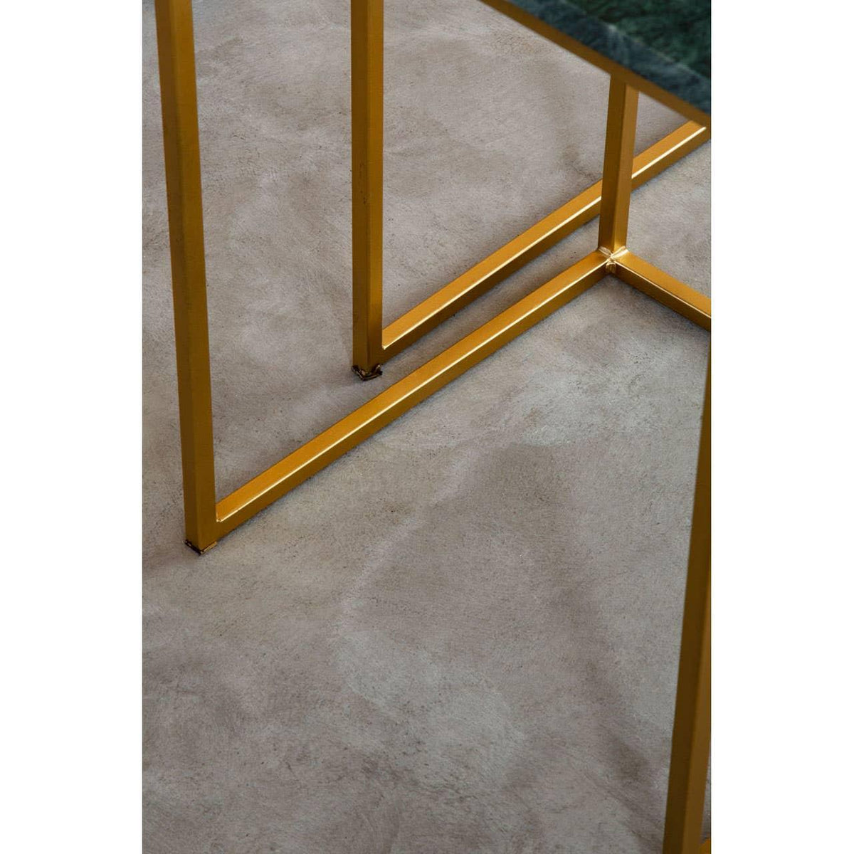 Gold metal table legs with green marble top detail on concrete floor