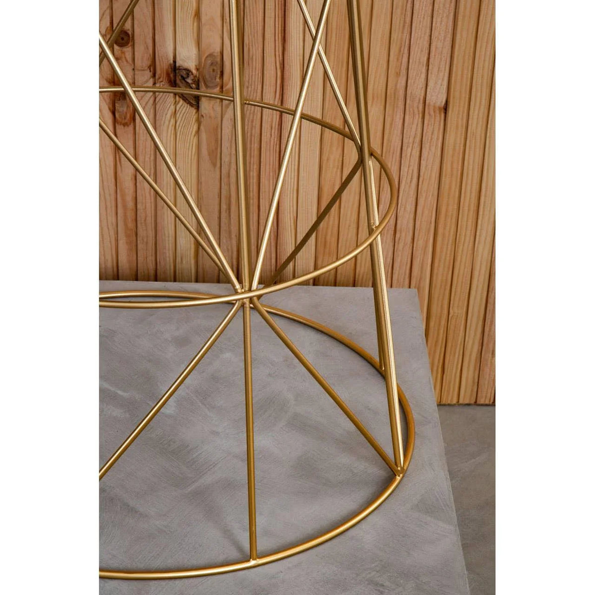 Gold metal table base with geometric design on concrete floor, wood panel background