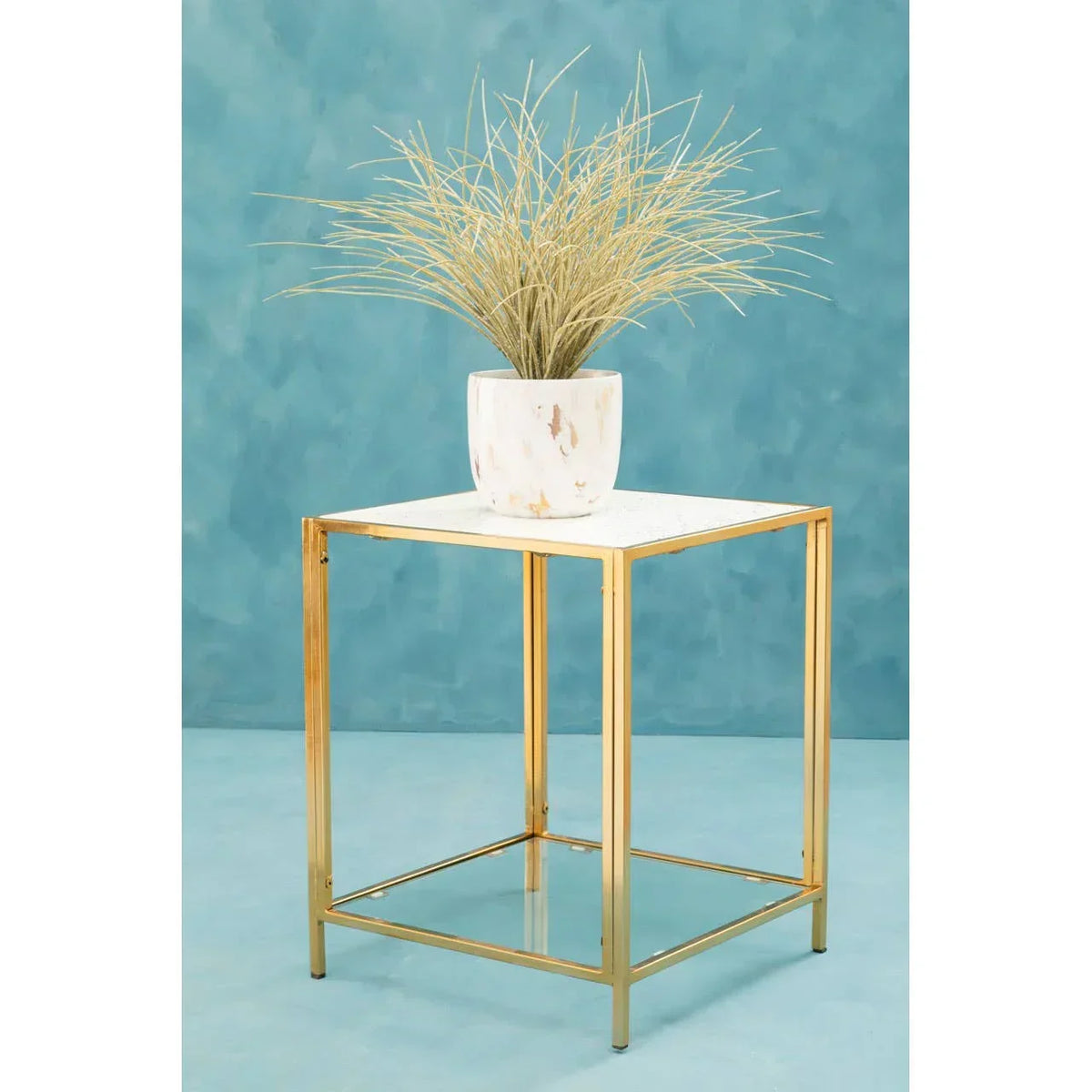 Gold metal side table with white marble top and potted plant against blue background
