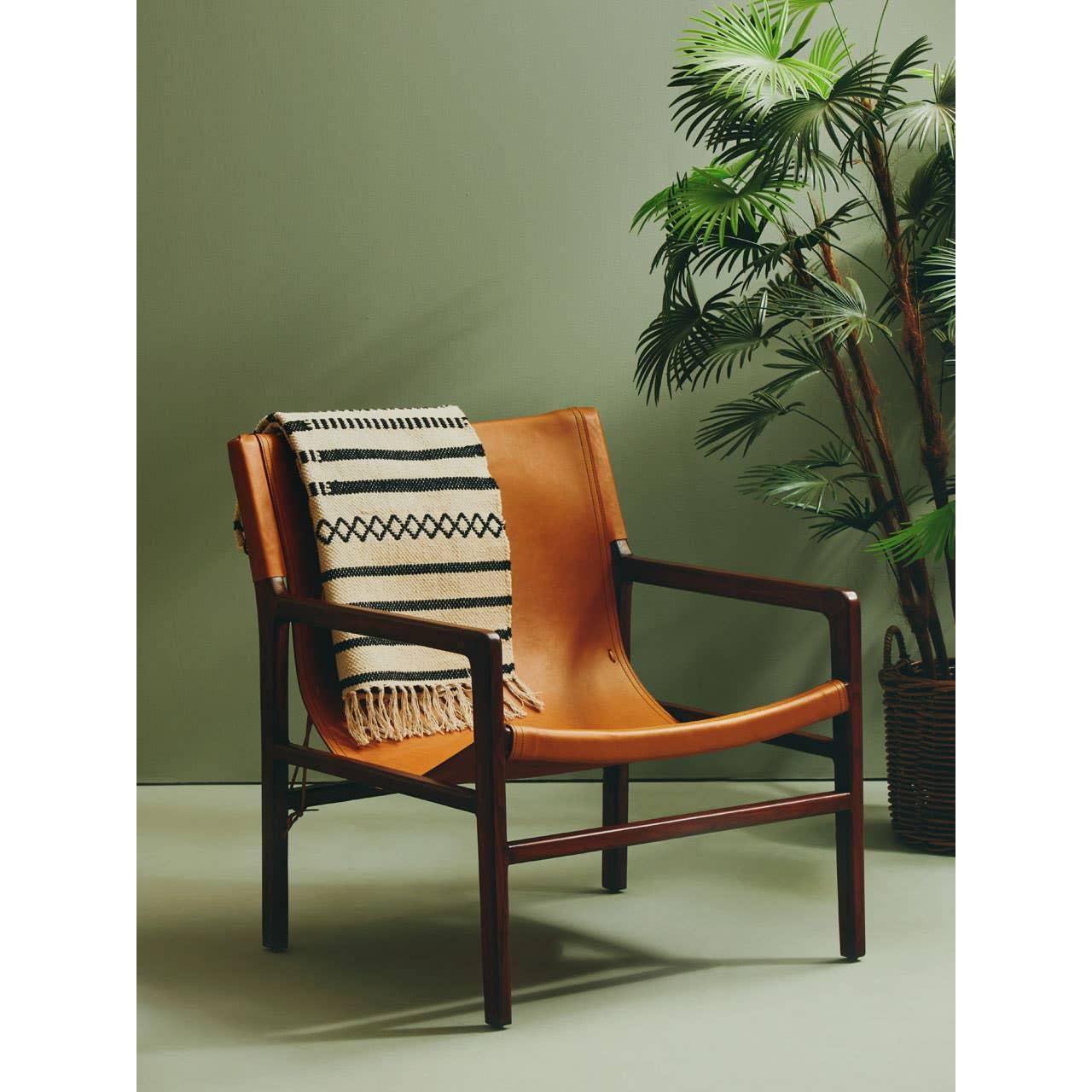Tan leather accent chair with dark wood frame and patterned throw, plant in background