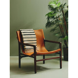 Tan leather accent chair with dark wood frame and patterned throw, plant in background