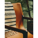 Tan leather accent chair with dark wood arms and woven throw in living room setting