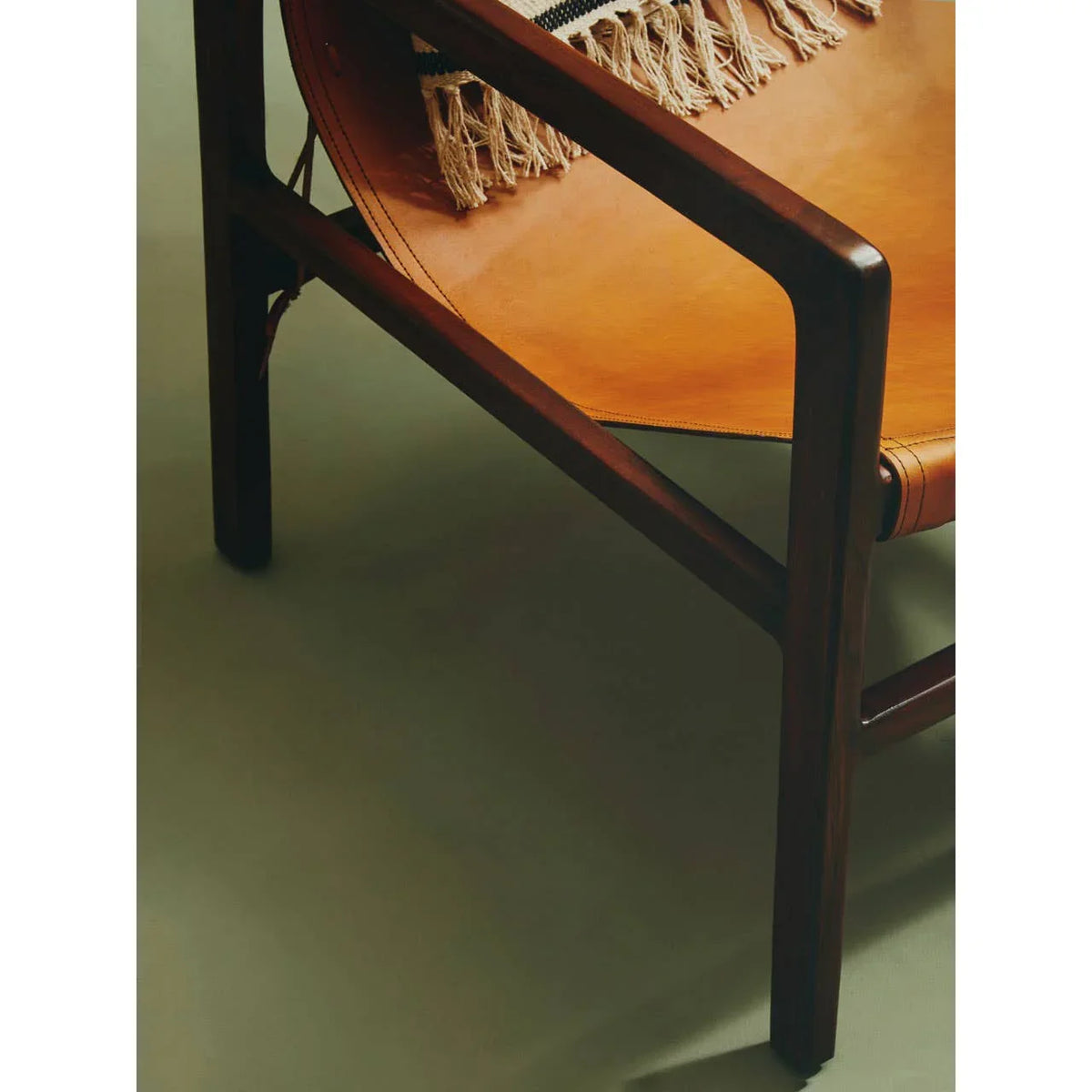 Close-up of wooden armchair with tan leather seat and woven fringe throw