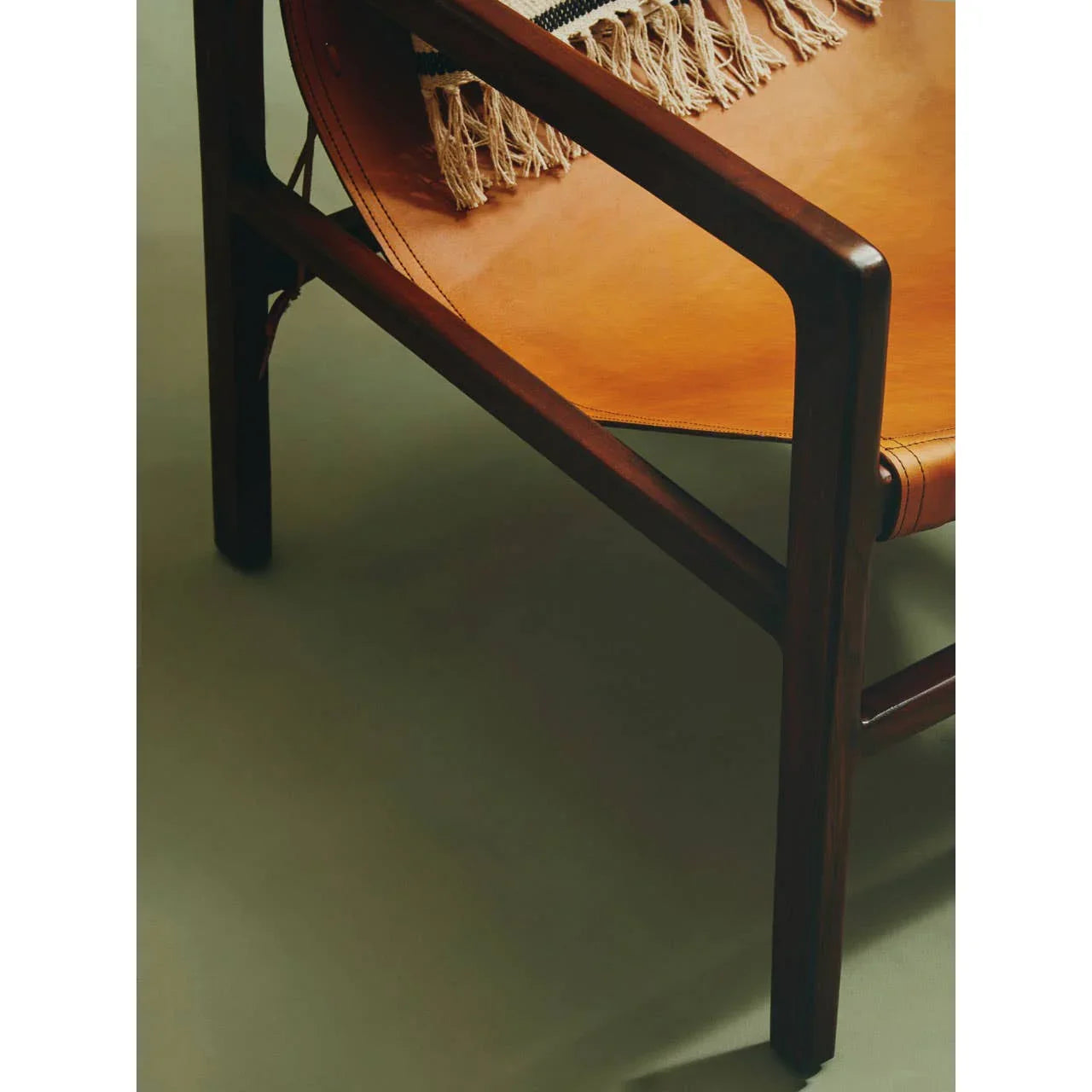 Close-up of wooden armchair with tan leather seat and woven fringe throw