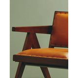 Closeup of wooden armchair with tan leather upholstery and studded trim against green wall