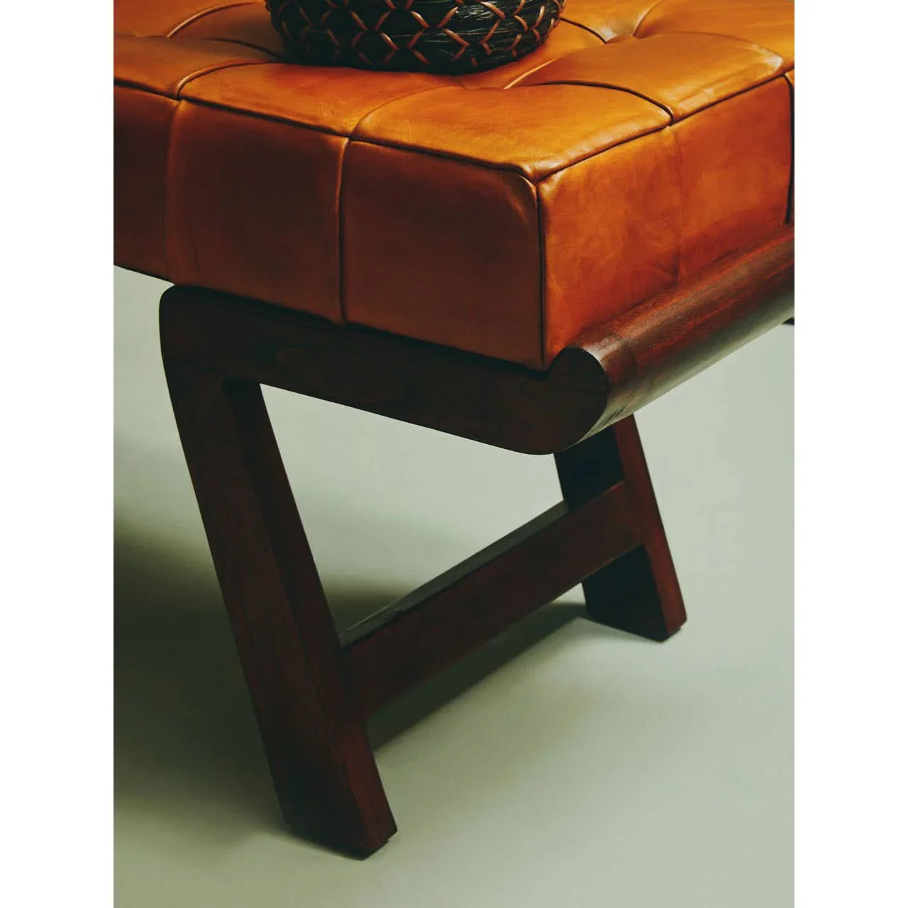 Corner of brown leather bench seat with dark wood legs and stitched cushion detail