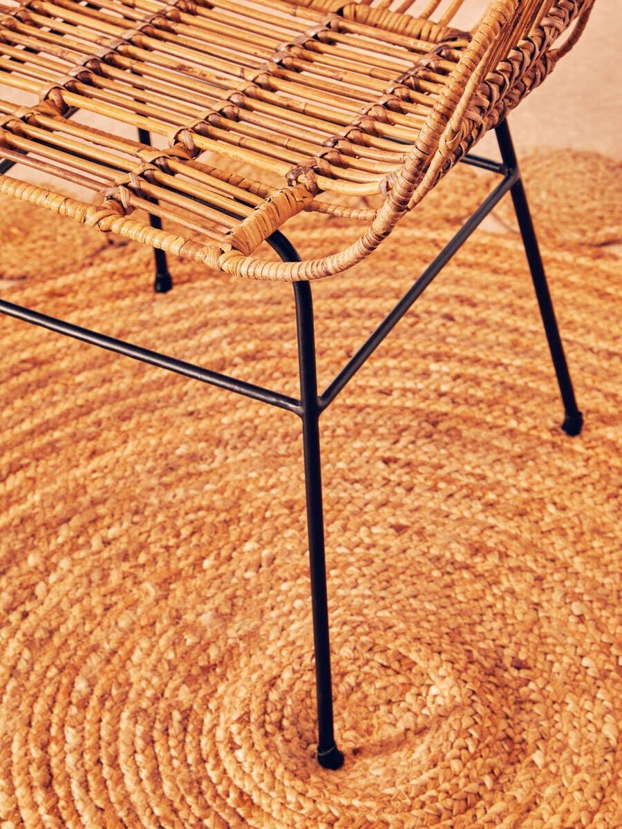 Rattan dining chair with black metal legs on woven jute rug
