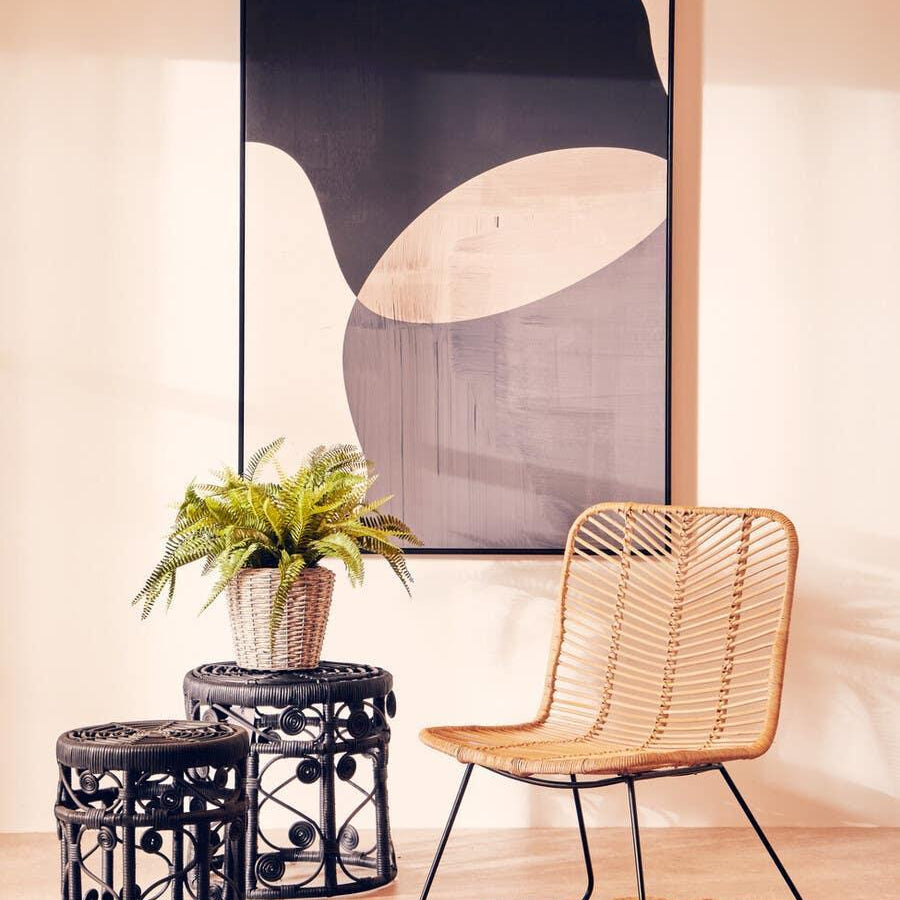 Rattan accent chair with black frame beside woven side tables and houseplant on jute rug