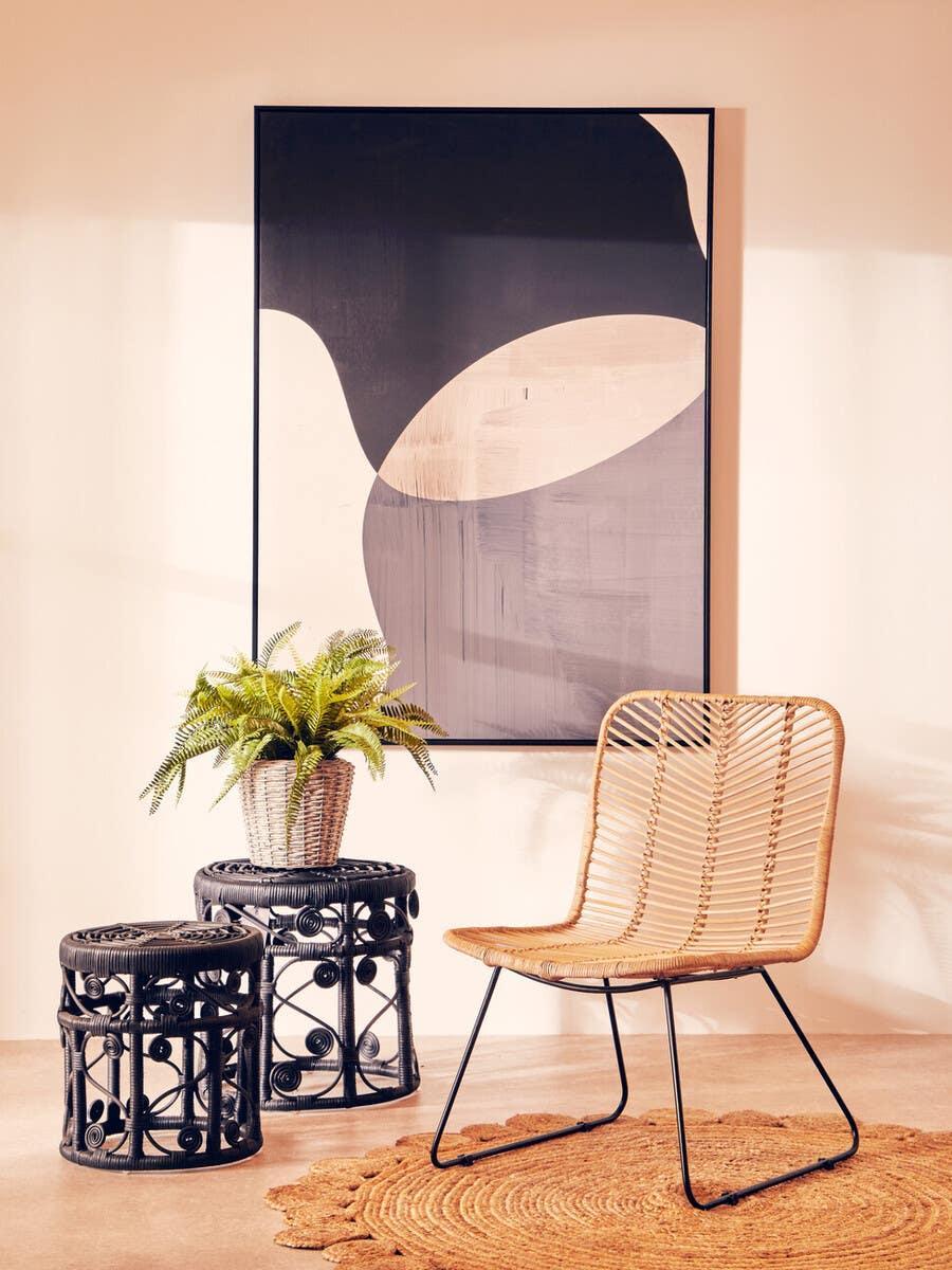 Rattan accent chair with black frame beside woven side tables and houseplant on jute rug