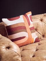 Brown leather Chesterfield sofa with tufted upholstery, featuring a colorful geometric patterned throw pillow resting on one of the seat cushions. The background is a dark wall, enhancing the sofa's modern design