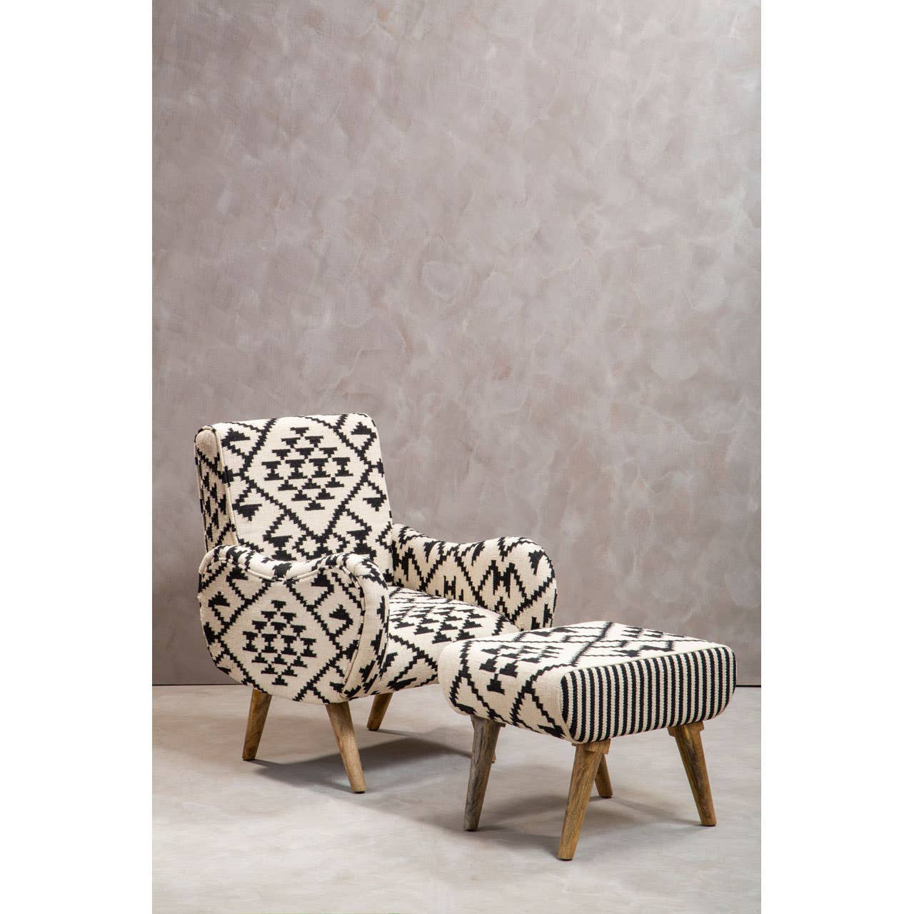 A Berber style footstool with a geometric patterned fabric in neutral tones, featuring wooden legs. The footstool is positioned next to a matching accent chair, both set against a textured light-colored wall