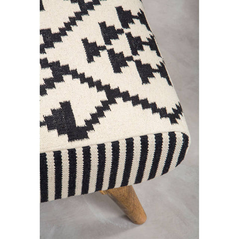 A close-up view of the Cefena Berber Style Footstool featuring a patterned fabric in black and cream with geometric designs, complemented by natural wooden legs. The footstool has a rectangular shape and a soft, textured surface