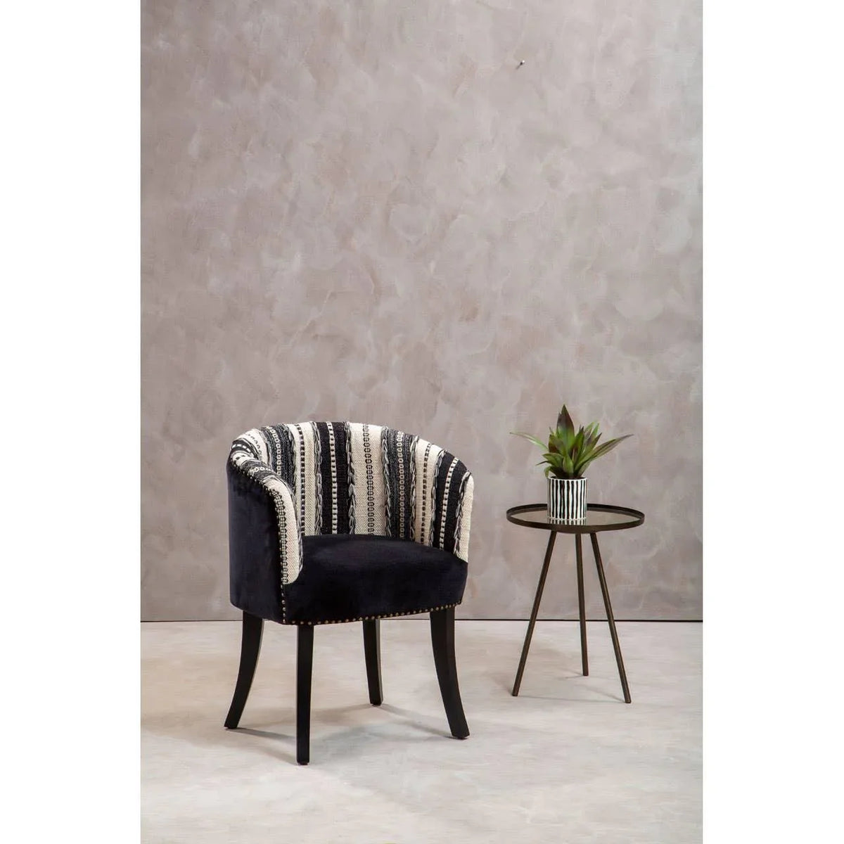 Patterned accent chair with black legs beside round black side table and potted plant